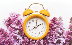 Yellow alarm clock and bouquet of pink lilacs on a white surface