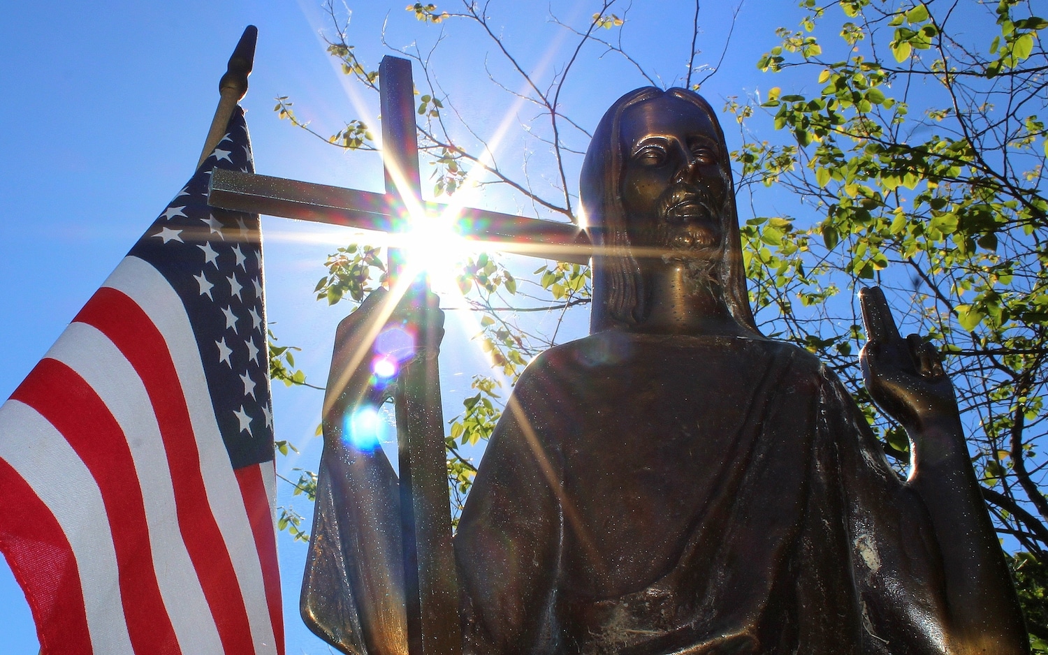 Sun shines through a statue of Christ on a grave marker alongside an American flag at St. Mary Catholic Cemetery in Appleton, Wis