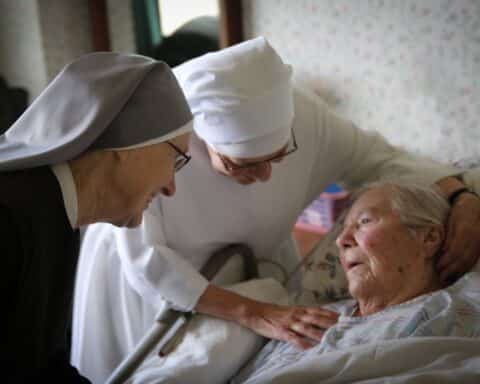 Two habited nuns care for an elderly woman.