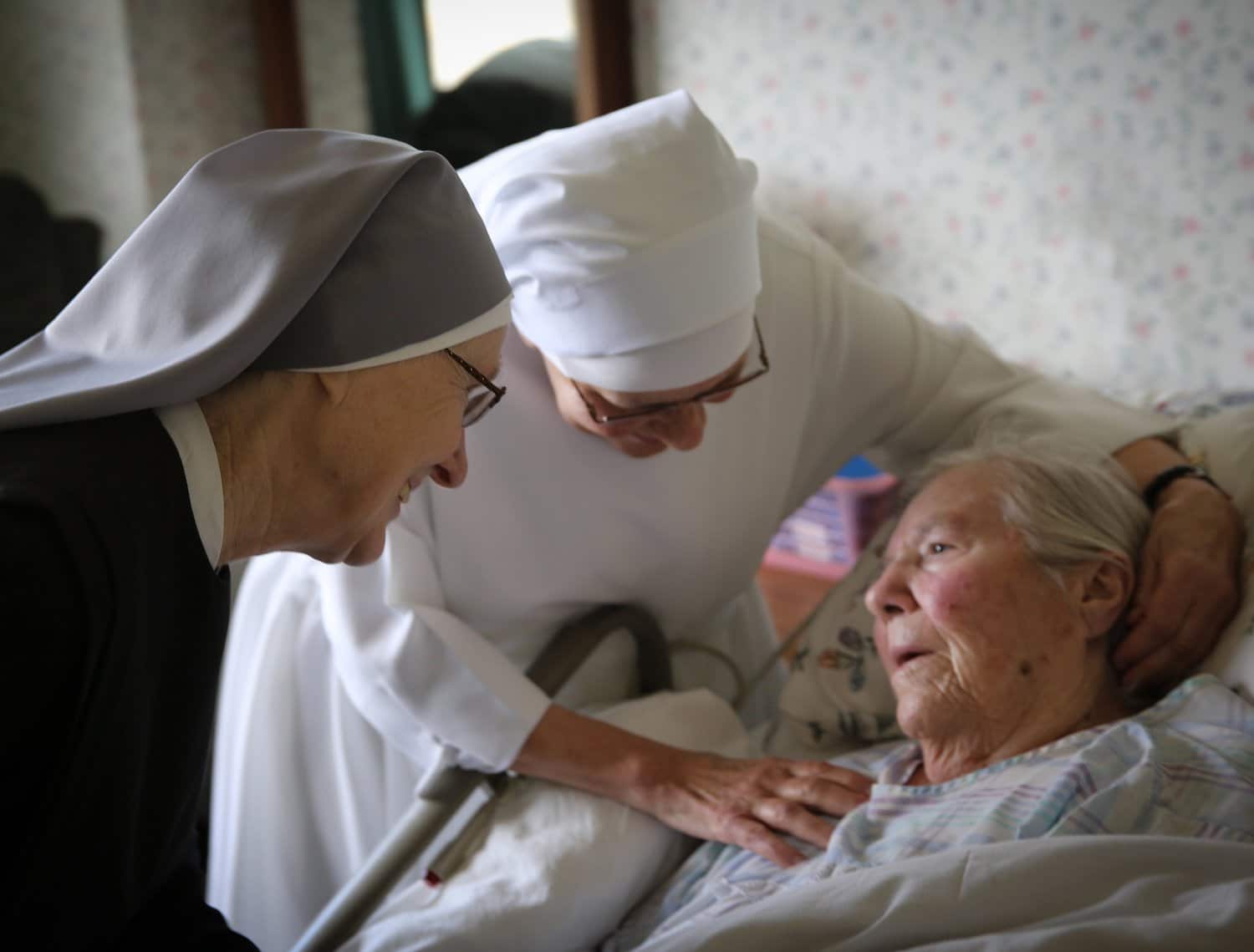 Two habited nuns care for an elderly woman.