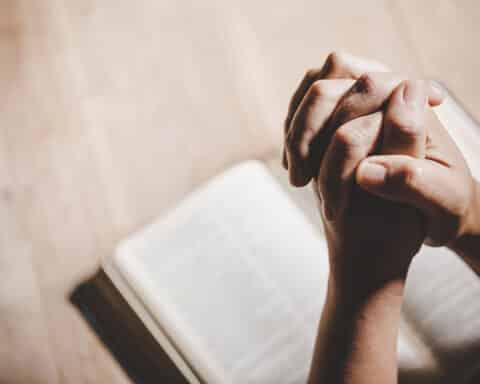 A photo of folded hands in prayer with a Bible in the background.
