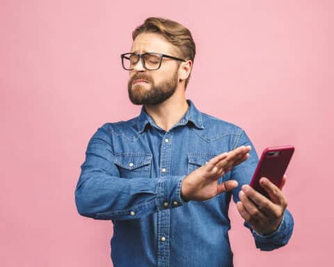 A man holds a smartphone away from his face, gesturing defensively