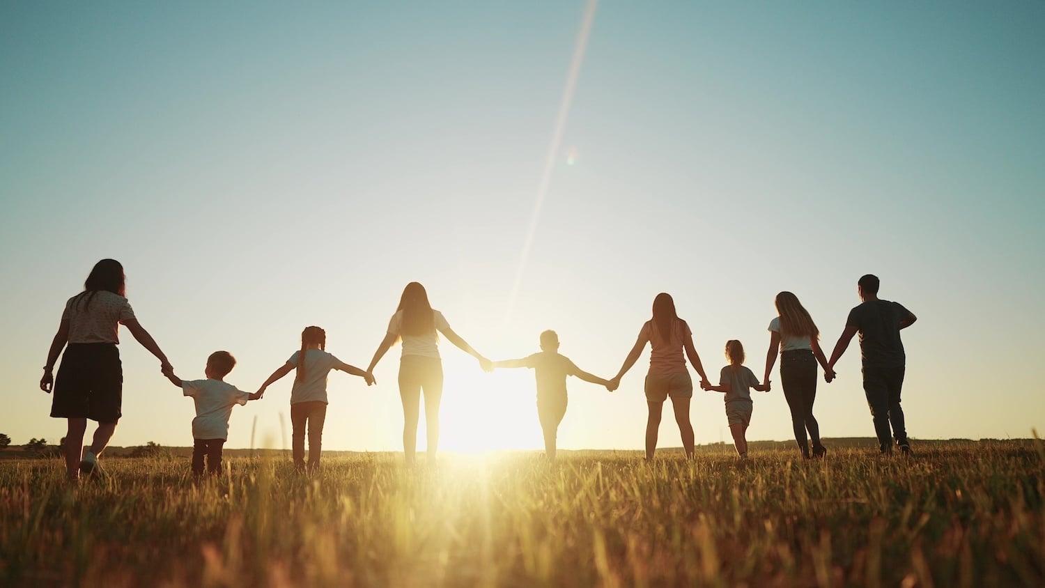 A large family holding hands is silhouetted against the sunset.