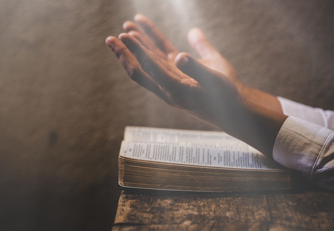 Hands reach out to Christ with a Bible in the background