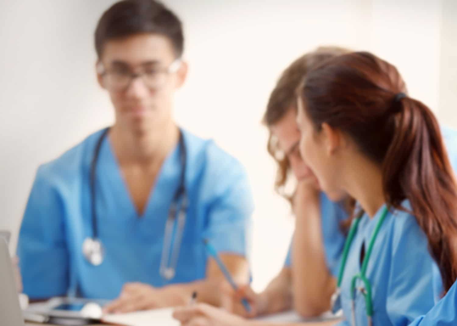 A photo of three medical school students in blue scrubs in class illustrating imposter syndrome.